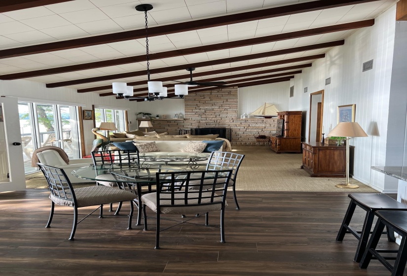 Vaulted ceiling with exposed beams, stone fireplace, wood-finish flooring, and a dining area with direct access to an exterior space