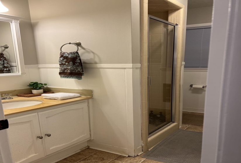 Bathroom featuring a single vanity with an integrated sink, a light-toned countertop, a shower enclosure with a glass door, and neutral-toned wall and floor tiling