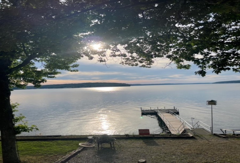 Waterfront property featuring a private dock with railings, a paved path, and established trees
