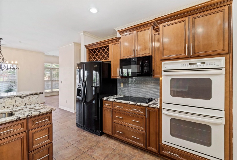 Kitchen featuring black appliances, brown cabinets, crown molding, light stone countertops, and light tile patterned floors