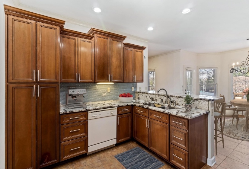 Kitchen with a peninsula, light stone countertops, dishwasher, decorative backsplash, and brown cabinets