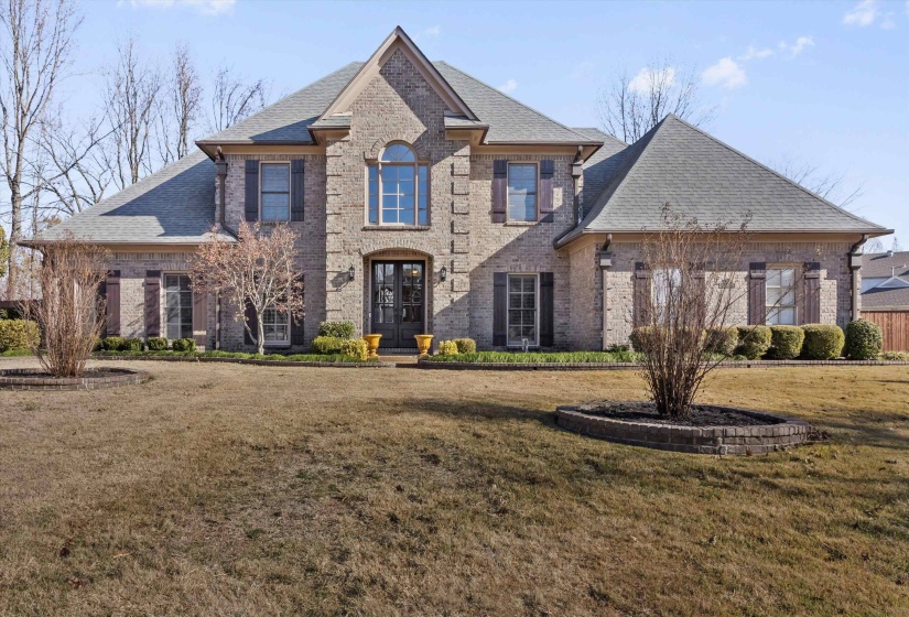 French country inspired facade with roof with shingles, brick siding, and a front lawn