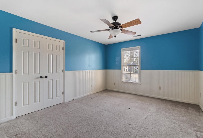 Unfurnished bedroom featuring a closet, wainscoting, carpet, and a ceiling fan