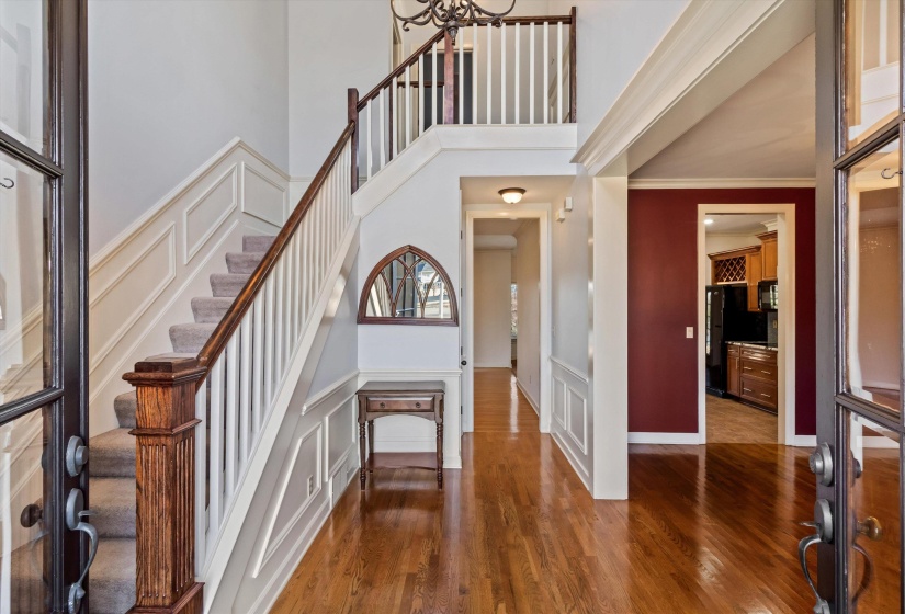 Entrance foyer featuring a decorative wall, dark wood-style flooring, wainscoting, a towering ceiling, and a chandelier