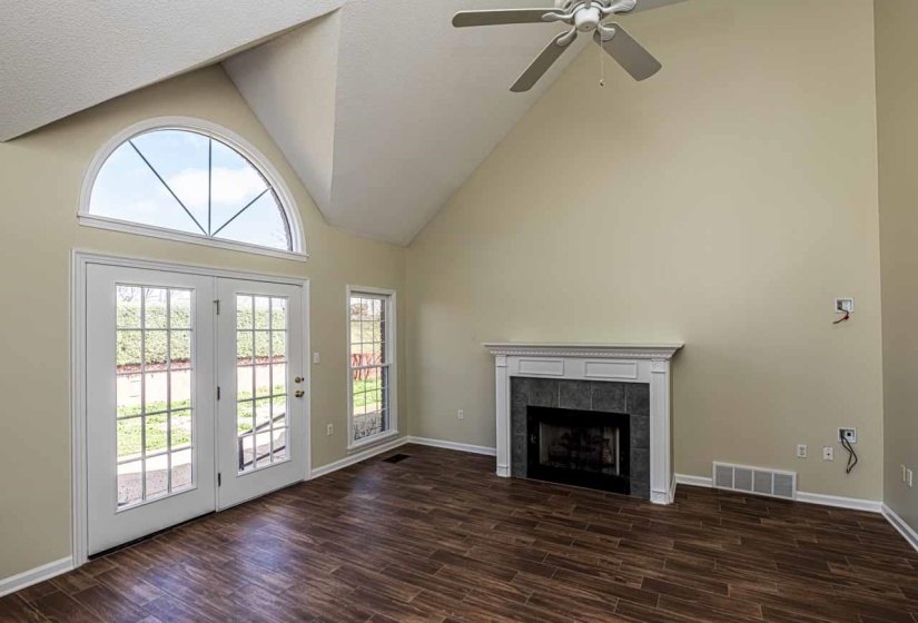 Unfurnished living room featuring vaulted ceiling, wood finish floors, a tile fireplace, and a ceiling fan