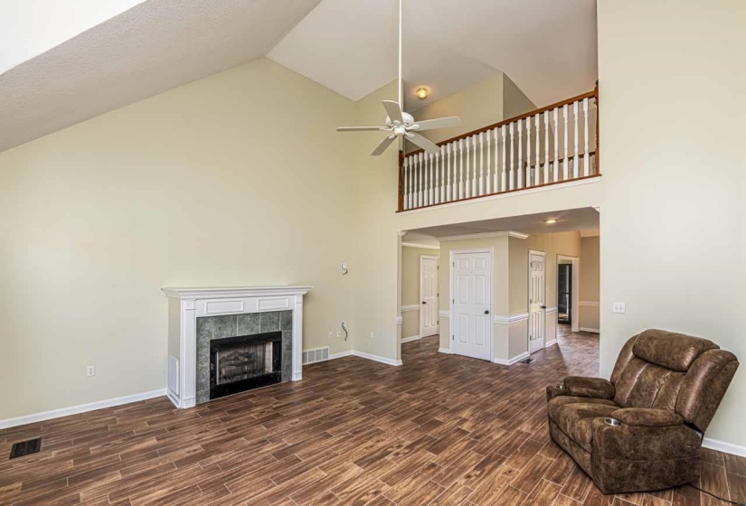Living room featuring wood tiled floors, ceiling fan, a tiled fireplace, and vaulted ceiling