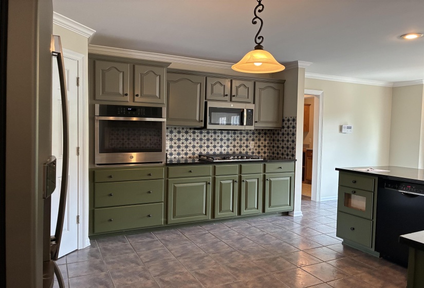 Kitchen featuring two-tone cabinetry, stainless steel built-in oven, stainless steel microwave, black countertops, and a patterned tile backsplash