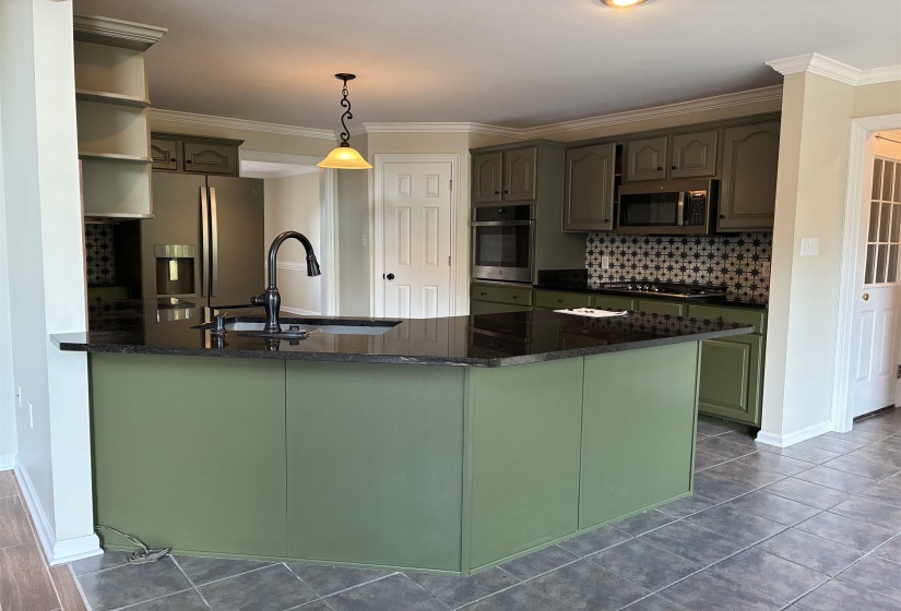 Kitchen featuring an island with a built-in sink and dark countertops, complement by cabinetry