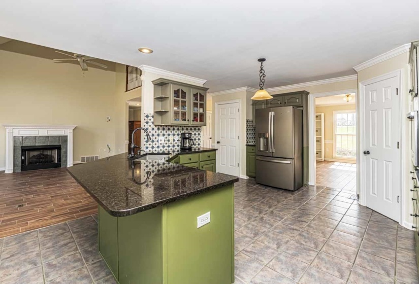 Kitchen featuring green cabinetry, stainless steel fridge, a fireplace, ceiling fan, and glass insert cabinets
