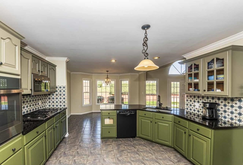 Kitchen featuring backsplash, a peninsula, glass insert cabinets, decorative light fixtures, and stainless steel appliances
