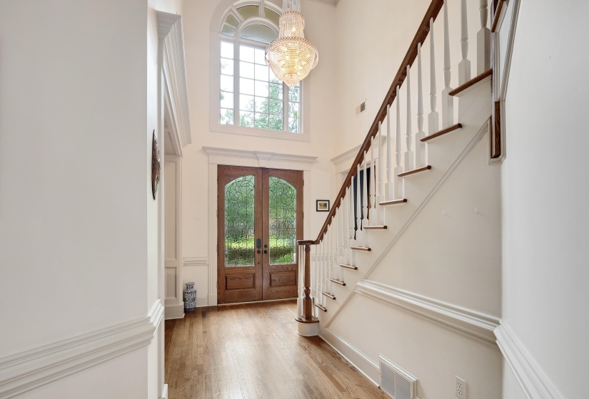 Two-story foyer featuring wood-finish flooring, a grand staircase with white risers and dark wood treads, and a statement chandelier above the entry