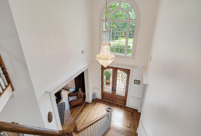 Two-story foyer featuring hardwood flooring, a grand chandelier, a large arched window, and double entry doors with decorative glass inserts