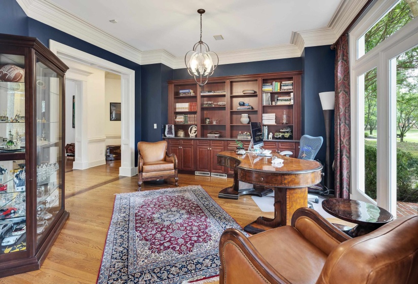 Spacious room with hardwood flooring, extensive built-in shelving, crown molding, and large windows