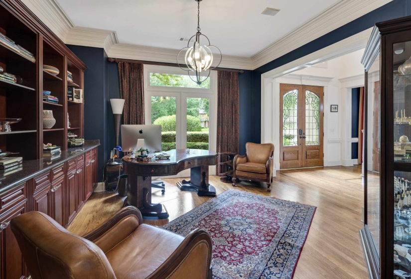 Hardwood flooring throughout this room, featuring a built-in wood-finish shelving unit, a large double-pane window, and a central chandelier