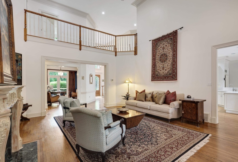 Two-story living area with hardwood flooring, a decorative fireplace with carved mantel, and an upper-level balcony featuring wood railings