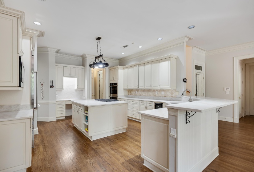 Expansive kitchen featuring wood-finish flooring, white cabinetry, integrated appliances, a central island with a cooktop, and a secondary island with a sink and breakfast bar