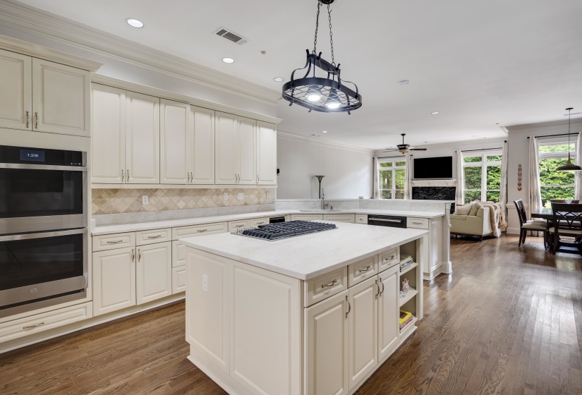 Kitchen featuring light-toned cabinetry, stainless steel double wall ovens, a center island with cooktop, and light-toned countertops