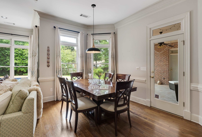 Dining space featuring wood-finish flooring, a contemporary pendant light fixture, multiple windows with extensive outdoor greenery, and a glass-paneled door