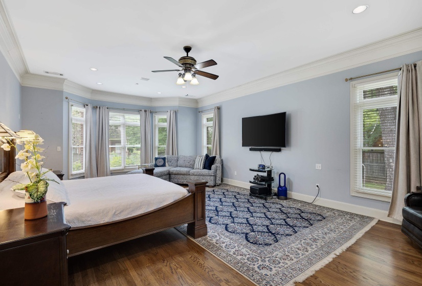 Spacious room featuring wood-finish flooring, a multi-windowed bay area, crown molding, a ceiling fan with integrated lighting, and recessed lighting