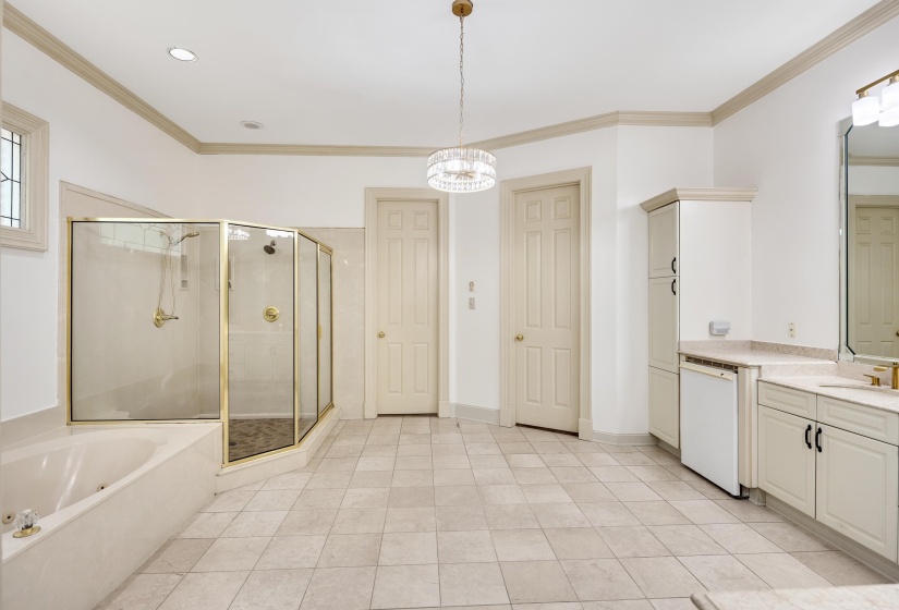 Spacious bathroom featuring a built-in tub, separate glass-enclosed shower with gold-tone fixtures, and dual vanities with integrated sinks