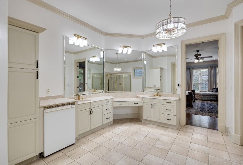 Spacious bathroom featuring light-toned tile flooring, extensive vanity cabinetry with integrated sinks, and a built-in makeup vanity