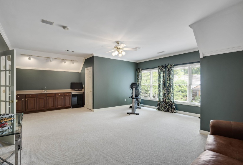 Spacious bonus room featuring an integrated wet bar with dark wood cabinetry, a ceiling fan, track lighting, and multiple windows