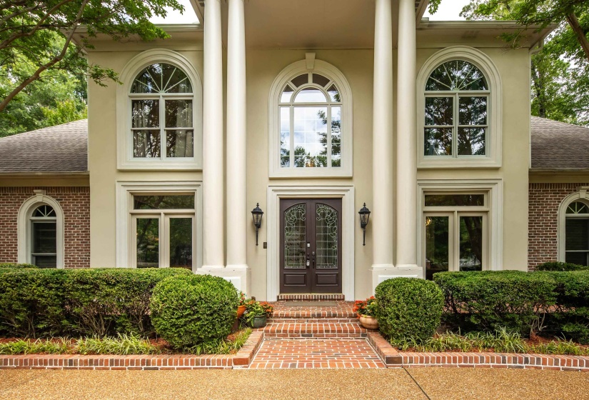 Stucco and brick facade featuring a double-door entry with decorative glass, flanked by large arched windows and substantial architectural columns