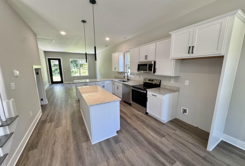 Kitchen featuring white cabinetry with dark hardware, stone-look countertops, stainless steel appliances, and a central island