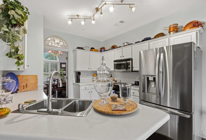 Bright kitchen featuring white cabinetry, stainless steel appliances, a double basin sink with a high-arc faucet, and light-toned countertops
