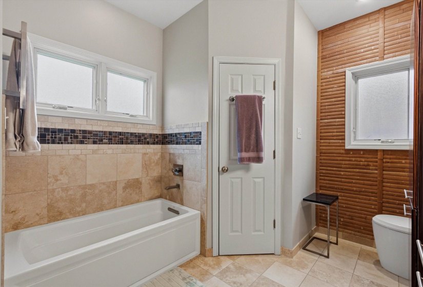 Bathroom featuring a built-in tub with tile surround, a mosaic tile accent band, and two windows above