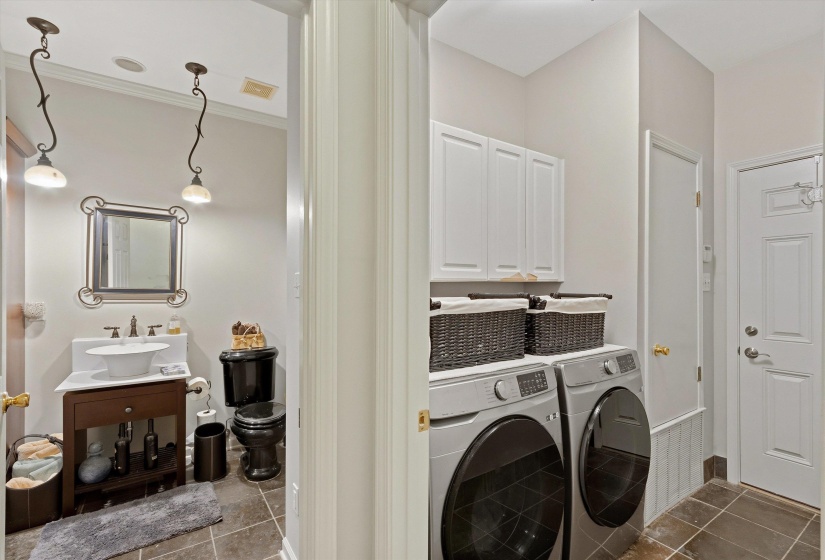 Functional laundry area with upper cabinetry and a side-by-side washer and dryer, adjacent to a powder room featuring a dark wood vanity with a vessel sink and a black toilet