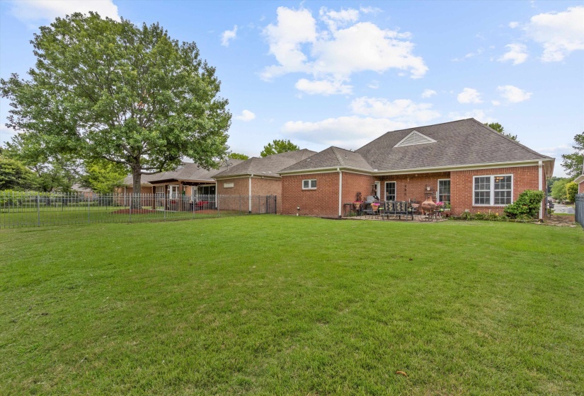 Expansive green lawn with a red brick exterior, a large mature tree, a paved patio area, and white-framed windows
