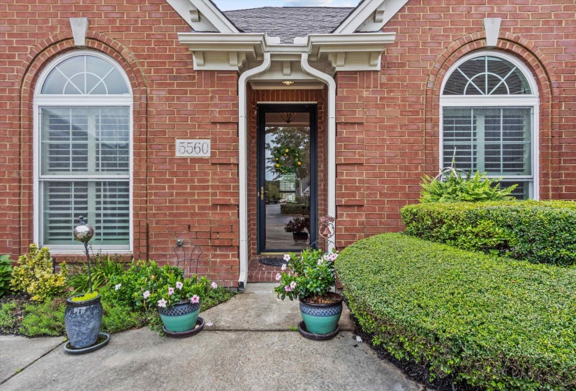 Brick exterior featuring a recessed entry, arched windows with decorative keystones, white window frames, and well-maintained shrubbery