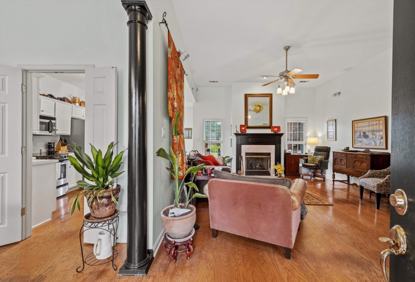 Living area featuring hardwood-style flooring, a fireplace with a black mantel, a ceiling fan with integrated lighting, and high ceilings