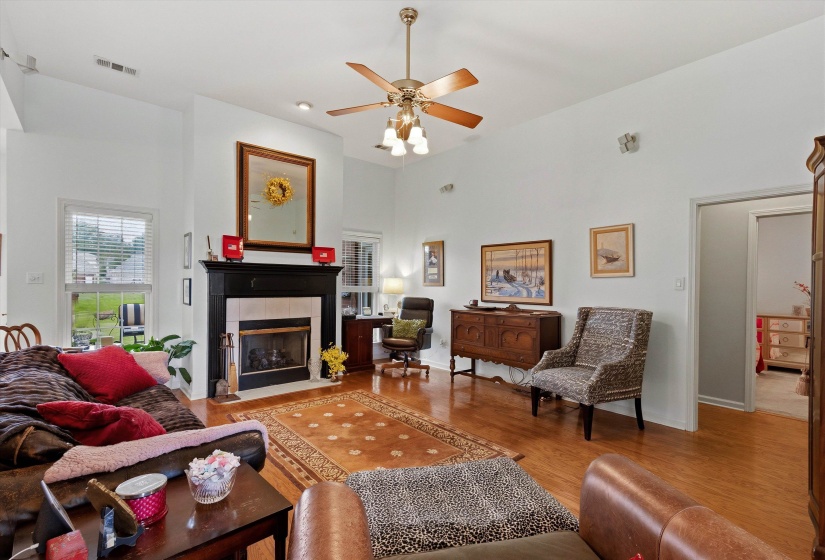 Living area featuring wood-finish flooring, a fireplace with a black mantel and white surround, and a ceiling fan