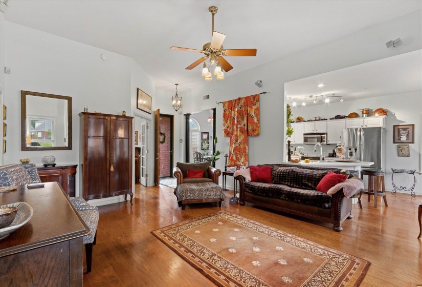 Living area with wood-finish flooring, vaulted ceilings, and a ceiling fan with integrated lighting
