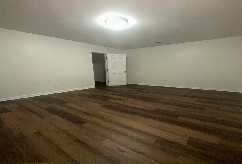 Spacious room featuring wood-finish flooring, light neutral wall tones, white baseboards, and a contemporary flush-mount ceiling light fixture