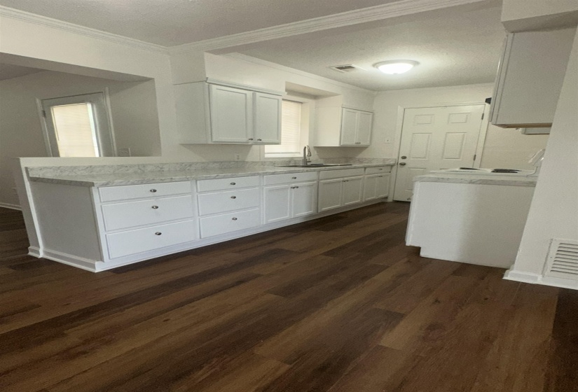 Kitchen featuring ample white cabinetry, a light-toned countertop, a stainless steel sink with a gooseneck faucet, and wood-finish flooring