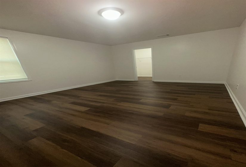 Spacious room featuring wood-finish flooring, light-toned wall finishes, and a flush mount ceiling fixture