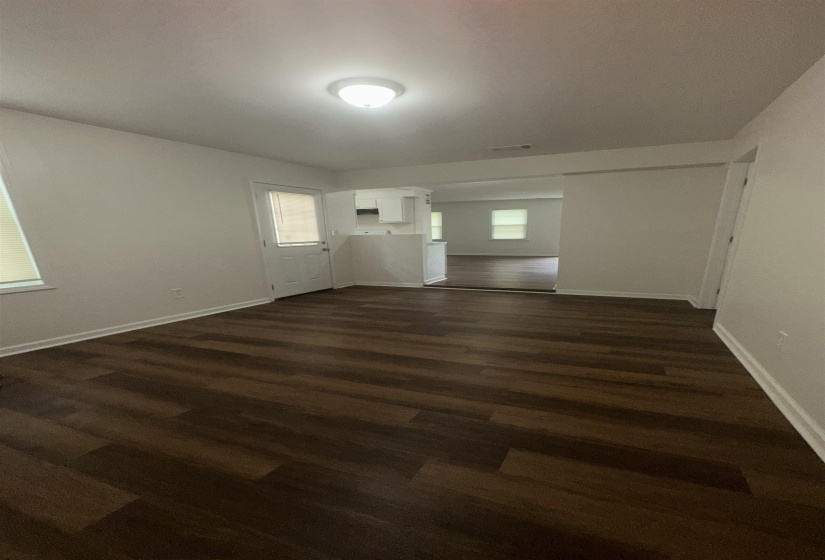 Spacious interior room featuring dark wood-finish flooring, white baseboards, and neutral wall paint