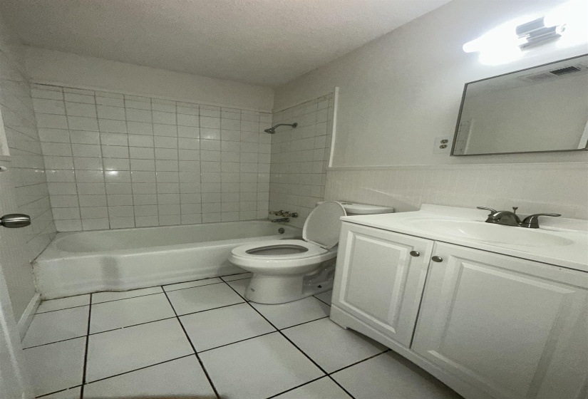 Full bathroom featuring a white tile floor, white tiled shower surround, and a white vanity with an integrated sink and chrome faucet