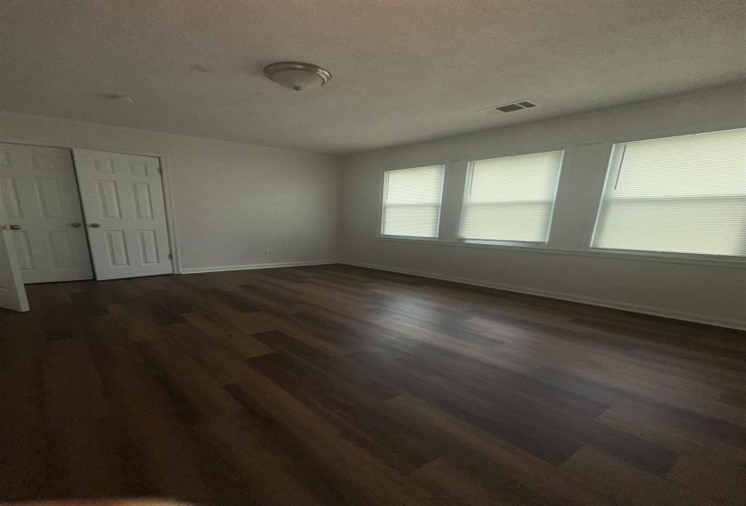 Room featuring wood-finish flooring, white walls, and multiple windows with blinds