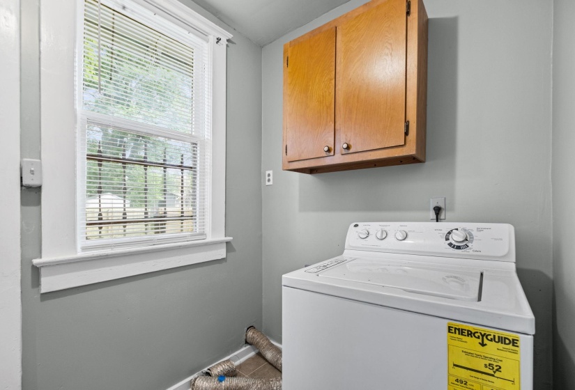 Bright laundry area featuring a window with white blinds, wood-finish cabinetry, and a neutral wall color