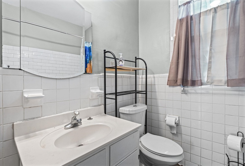 Bathroom featuring white square tile walls, a vanity with an integrated sink, a rectangular framed mirror, and a window with sheer curtains