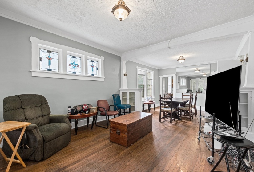 Spacious living area featuring hardwood flooring, crown molding, built-in cabinetry, and decorative stained-glass transom windows
