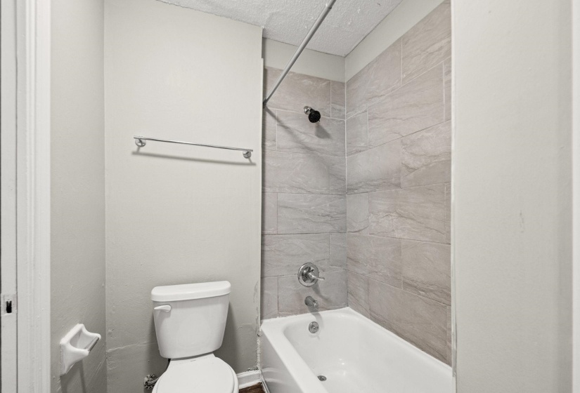 Full-size bathtub with a chrome faucet and shower head, surrounded by light gray tiled walls