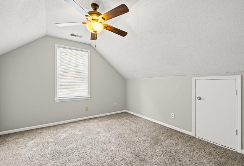 Carpeted room with a ceiling fan, sloped ceiling, single window with blinds, and a white interior door