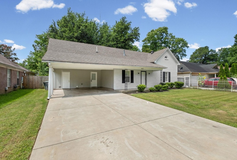 White exterior residence featuring a covered carport, elongated concrete driveway, and a front lawn with established landscaping
