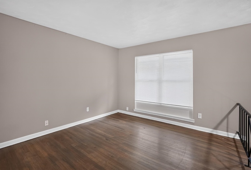 Expansive room featuring wood-finish flooring, neutral-toned walls, a large window with horizontal blinds, and white baseboards