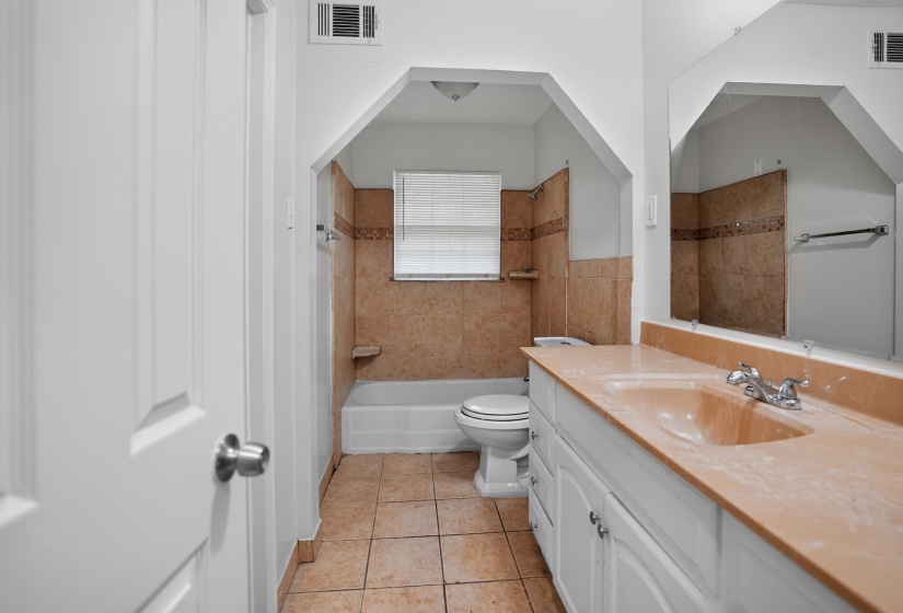 Bathroom featuring a vanity with an integrated sink and chrome faucet, a large wall-mounted mirror, and tile flooring
